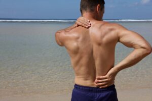 man with back pain in a swimsuit by the beach