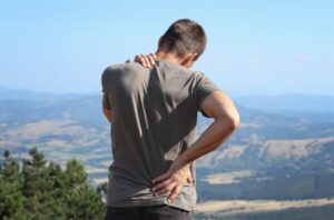 man taking a hike holding his back and neck in pain