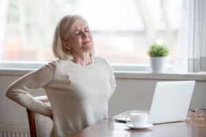 older woman feeling back pain while working at a laptop
