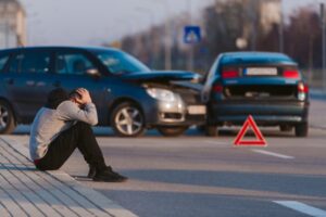man sitting next to wrecked car on the phone